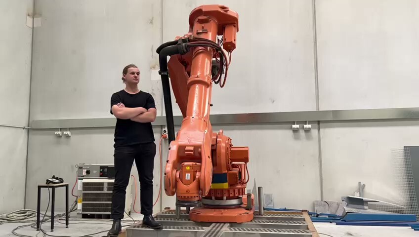Tom Macrokanis standing beside a large industrial robot